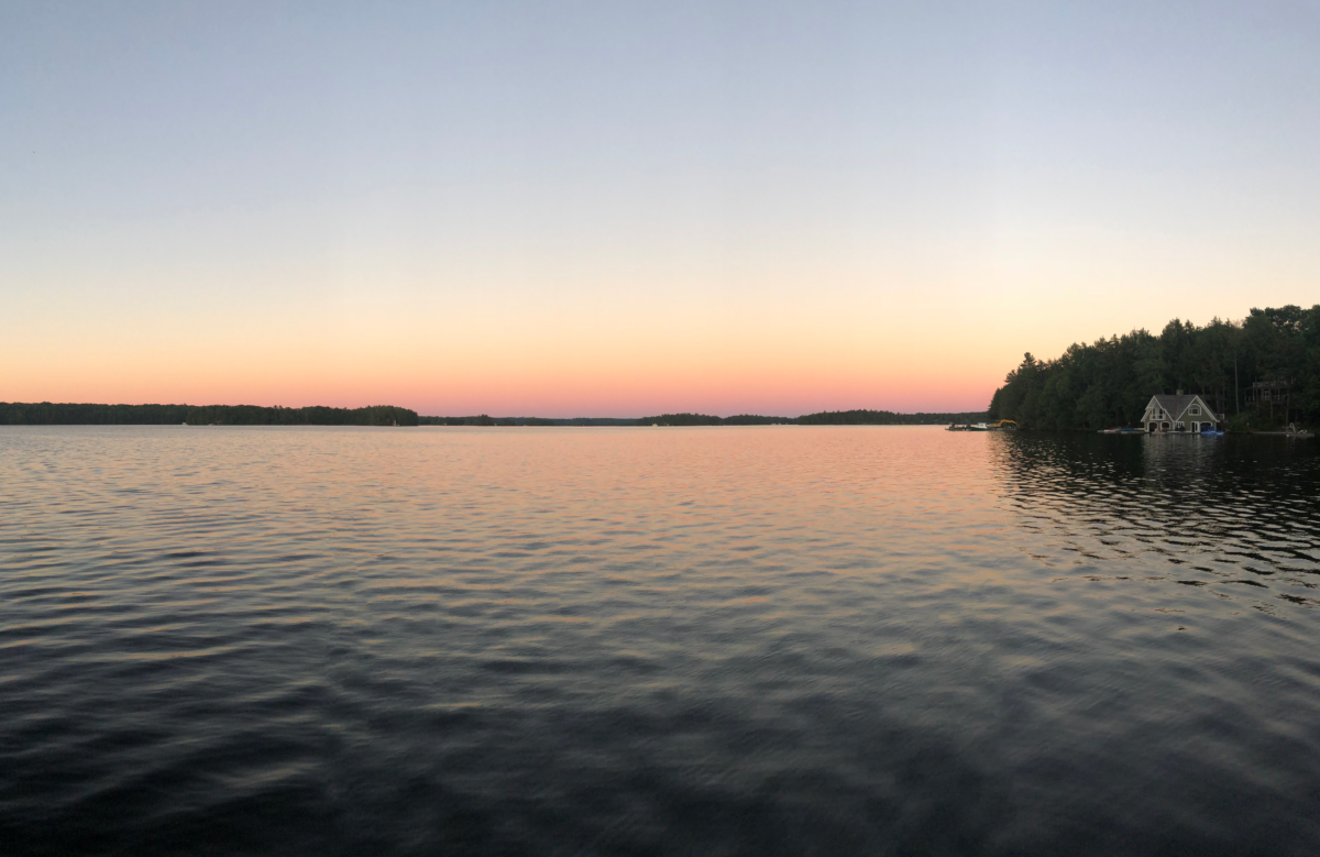 an orange sunset over a lake. There is lad in the distance and a small piece of land poking out on the right side of the photo.