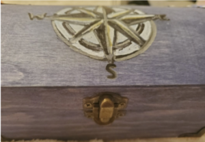 a wooden box with a brass clasp and a picture of a compass on top.