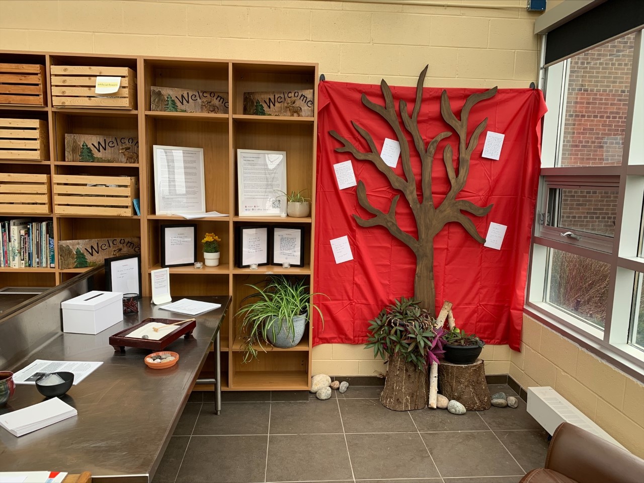 a photo of the reflection room, a table with writing supplies and a red cloth hanging on the wall with a tree and peoples' written memories and reflections on grief posted on the sheet around the tree.