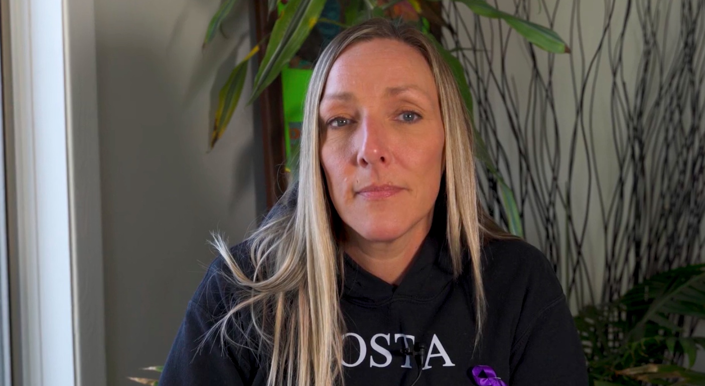 a white woman with long, blonde hair wearing a black sweatshirt stairs into the camera.