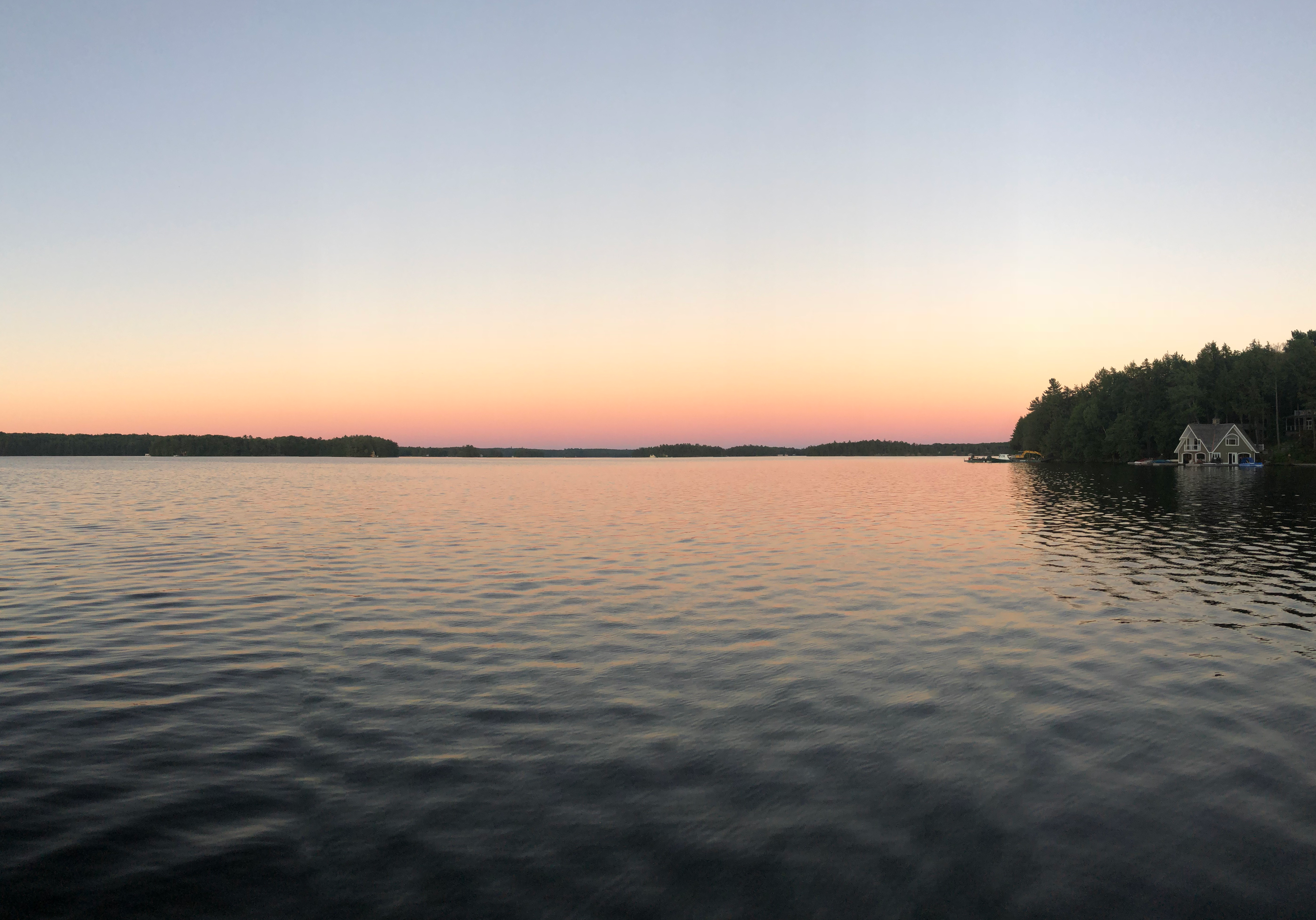 an orange sunset over a lake. There is lad in the distance and a small piece of land poking out on the right side of the photo.